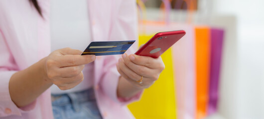 Hands of woman sitting on sofa using smart phone shopping online with credit card while paper bag on couch, happy female paying with transaction financial, purchase and payment, business concept.