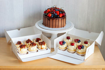 Chocolate cake decorated with fresh berries, strawberry, cherry and blueberry and box of assorted cupcakes on a table