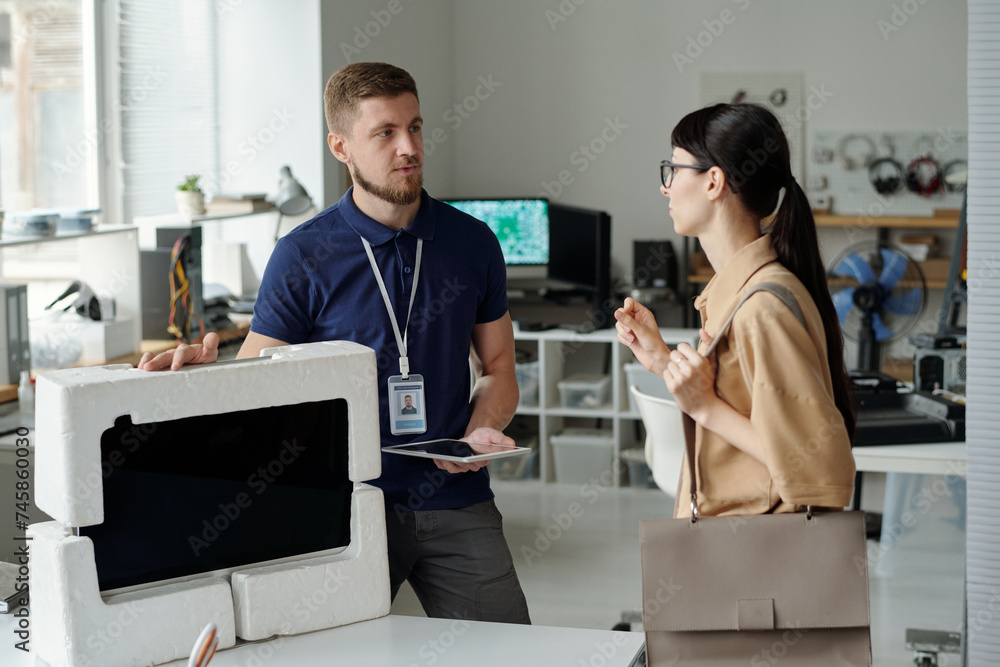 Poster young confident manager of troubleshooting center looking at female client handing over desktop comp