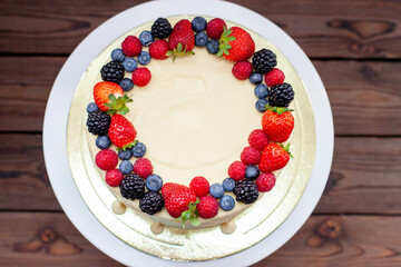 Cheesecake with fresh strawberry, raspberry, blueberry and blackberry, melted white chocolate on rustic wooden cakestand and background