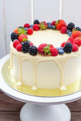 Cheesecake with fresh strawberry, raspberry, blueberry and blackberry, melted white chocolate on rustic wooden cakestand and background