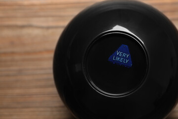 Magic eight ball with prediction Very Likely on wooden table, closeup