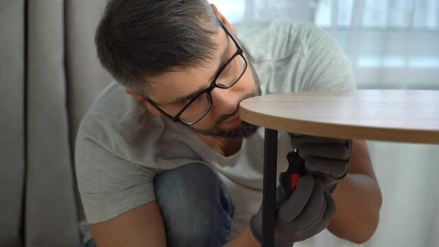 Close up of man assembles wooden oak coffee table using screwdriver at home. Process of assembling furniture