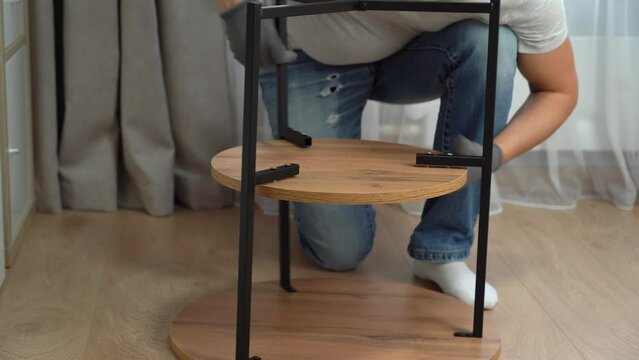 Male hands assemble wooden oak coffee table using screwdriver at home. Process of assembling furniture