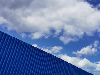 Fototapeta na wymiar Blue metal plate against blue cloudy sky. Siding. Seamless surface of galvanized steel. Industrial building wall made of corrugated metal sheet, flat background photo texture.