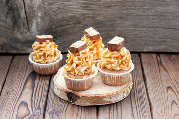 Delicious chocolate cupcakes with peanut butter frosting, chocolate bites and salted caramel sauce on rustic wooden background