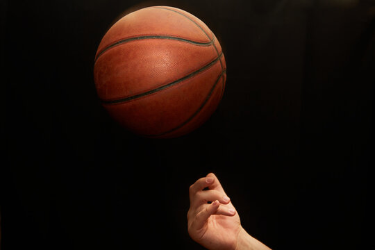 A hand tosses a basketball upwards on a black background, close-up, the start of the game, sports background.