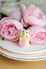 Edible hamster made of white chocolate holding a strawberry. Peonies and candles on the background