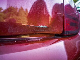 Close-up of a dented hatch with damaged paint on car in parking lot.