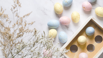 Colorful Easter eggs with golden spots in a wooden box on a white marble background and some flowers.