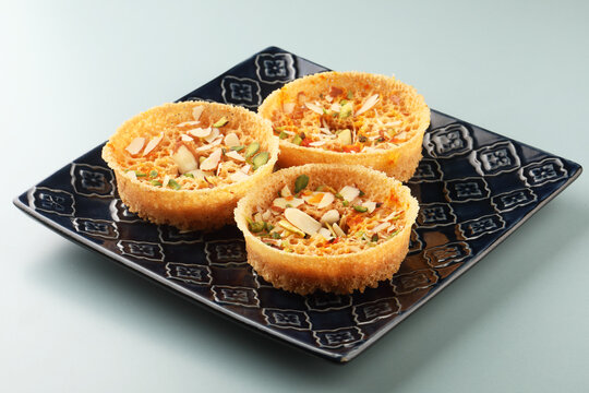 Rajasthani Ghevar. Ghewar is an Indian crunchy sweet dish made using refined flour, sugar, and ghee. Garnished with silver foil and dry fruits.