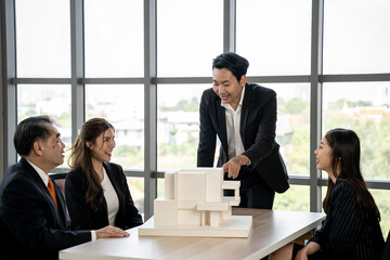 Asian businessman talking with team in meeting room. They dissing about building model and design together.	