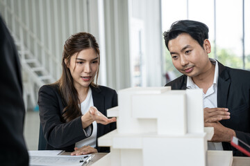 Asian business woman presenting building model with team in office. They dissing about building model design together.
