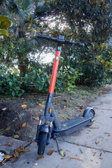 Dockless stand-up electric scooter on a kick stand on a pedestrian sidewalk in a shade of trees