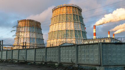 Large cooling towers of thermal power plants are located behind a concrete fence with barbed wire....