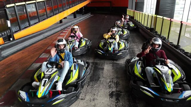 aerial drone view over a group of young racers wearing helmets on an indoor karting track waving at the camera ready to start the race