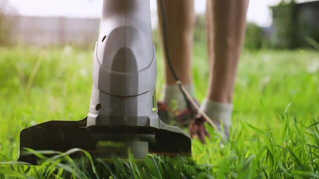 Close-up of an electric lawn trimmer in action. The working part of the trimmer cuts green grass. Background image illustrating the work of a gardener