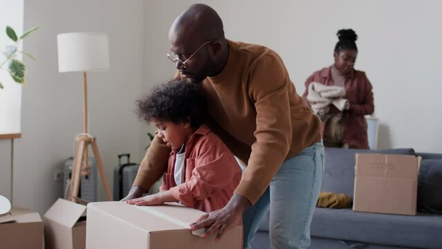 African American father and little son sealing box with stuff in living room while packing belongings for moving