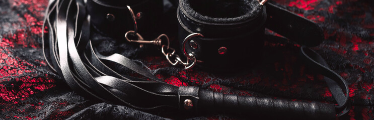 set of BDSM sex toys with handcuffs and whip flogger for submission and domination on a black background. Wide header cover for banner for sex shop - obrazy, fototapety, plakaty