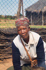 village old african woman standing in front of a thatched hut.