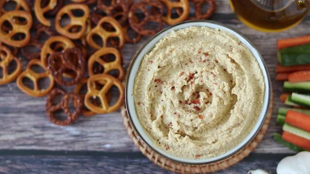 Hand sprinkling red pepper flakes on chickpea hummus dip. Top view. 