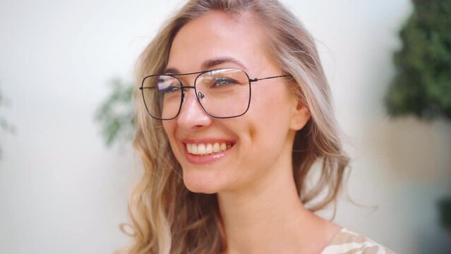Confident woman wearing stylish eyeglasses and looking away. Closeup portrait of beautiful blond lady in glasses looking at camera. Zoom in shot of attractive young lady against blurred background.