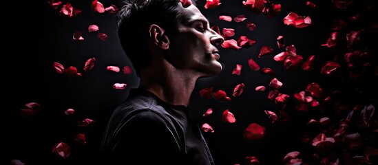Man Surrounded by Red Rose Petals on Mysterious Black Background - obrazy, fototapety, plakaty