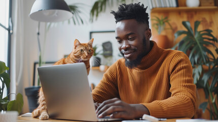 young black man with laptop sitting on desk in home office, pet accompanied on his laptop. Friendship between cat and owner. Best friends.  - obrazy, fototapety, plakaty