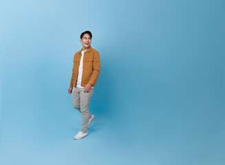 Fototapeta na wymiar Full body smiling happy young Asian teen man walking going strolling and looking sideways isolated on blue background studio portrait.
