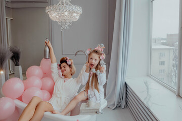 Mom and daughter in pink pajamas and curlers having fun in bathroom