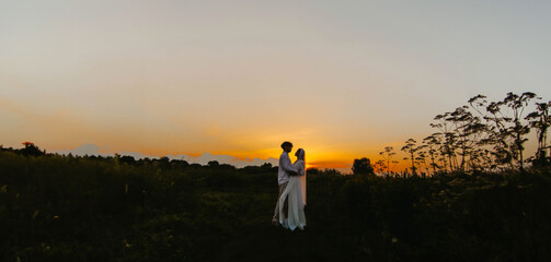 Obraz premium silhouettes of a newlywed couple in love in a field at sunset. Outdoor wedding in summer