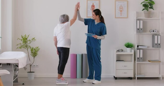 Senior woman weight measurement on floor scales, getting good result, nurse congratulations. Old woman during examination, regular check, monitoring elderly person body mass, loss of weight, slimming