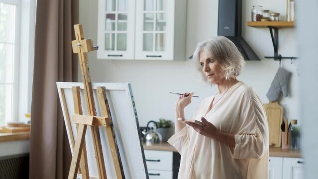An elderly female artist painting a picture on canvas