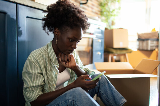Woman using smartphone on floor with moving boxes around
