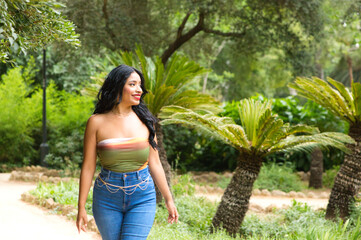 Young and beautiful Latin woman from South America walks among the trees and vegetation of the park. The woman is smiling and happy and is posing for photos. Travel and holiday concept.