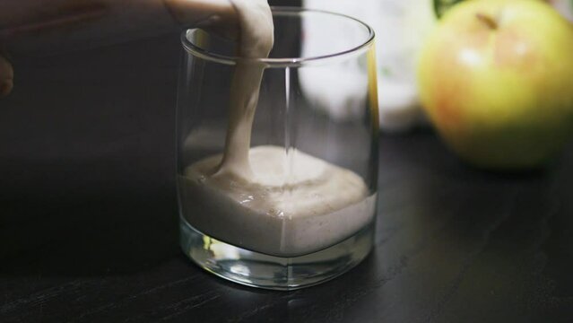 Pouring thick greek yoghurt oatmeal and apple smoothie into glass. Close up.