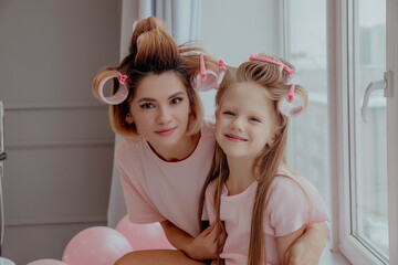 Portrait of mom and daughter in pink pajamas and curlers - obrazy, fototapety, plakaty