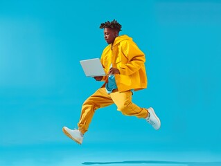 A young man jumping with open laptop in his hand on a blue studio background