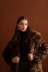 Fashionable confident woman wearing hat, trendy faux fur leopard print coat, posing on brown...