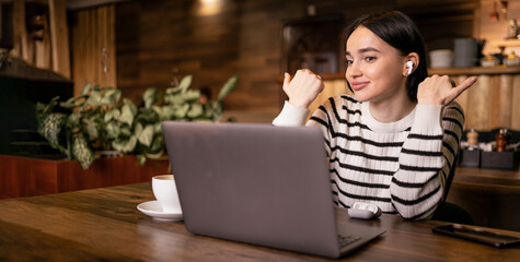 Positive young woman having video conference on laptop talking and gesturing on web camera sitting in cafe. Online tutoring