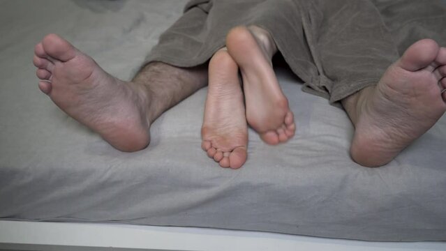 An intimate shot of a couple's feet hiding under the covers on a bed. Concept of tenderness, affection, and relationship