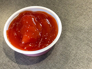 Ketchup in a plastic ramekin on a gray background