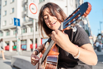 young woman singer-songwriter singing and playing guitar in the street to promote her album.