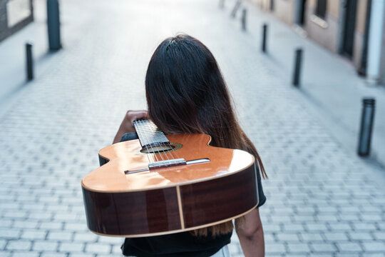 unrecognizable woman walking through the city with an acoustic guitar on her shoulder