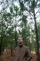 A young man standing alone in a forest looking at the trees. Below View