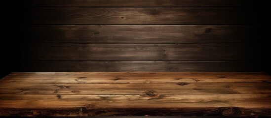 An aged wooden tabletop sits in a dark room, creating a stark contrast between the dark surroundings and the lighter wood. The surface of the vintage dining table shows signs of wear and age. - obrazy, fototapety, plakaty