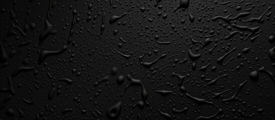 Numerous water drops are scattered across a black, plastic grainy abstract background. The drops reflect light, creating a striking contrast against the dark surface. - obrazy, fototapety, plakaty