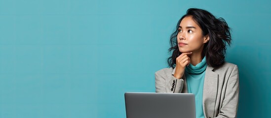 A focused woman, of Asian descent, sits in front of a laptop computer, deeply engrossed in her work. She appears contemplative, occasionally looking away as if pondering decisions to be made.