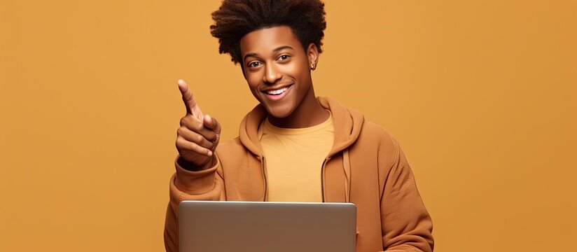 A happy African American teenager student boy is holding a laptop computer and pointing at the screen. He is presenting online education courses or webinars, showcasing e-learning opportunities.