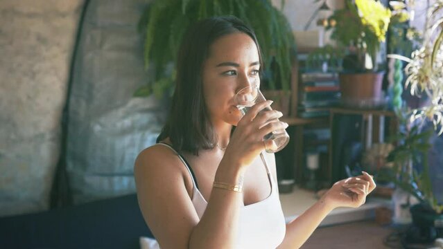 Pills, glass and woman drinking water for medicine, healthcare and wellness of sick person. Smile, medical and Asian girl with supplements, pharmaceutical drugs and prescription capsule for diet